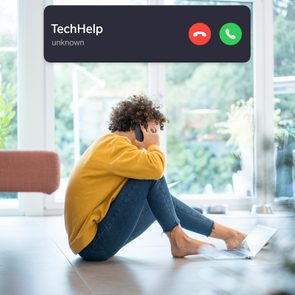 Person on phone, sitting on floor with laptop, receives unknown call labeled 