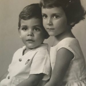 Two young children sit closely together, looking towards the camera, in a black and white studio portrait.