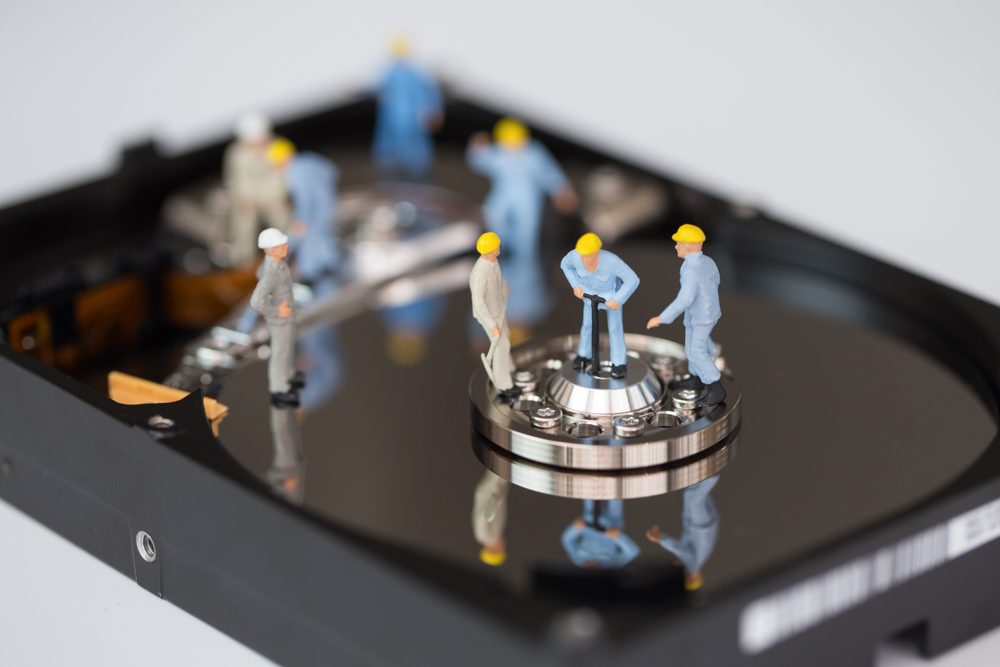 Miniature construction workers stand on a hard drive platter, appearing to perform maintenance tasks, creating an imaginative scene.