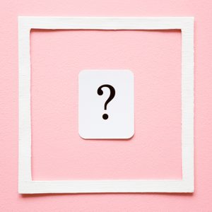 White card featuring a black question mark, centered within a white square frame, set against a pink background.