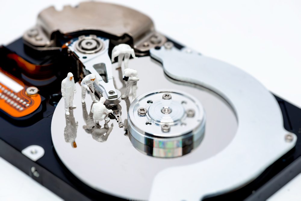 Miniature figures inspect components on an open hard drive platter, resembling a futuristic workspace.