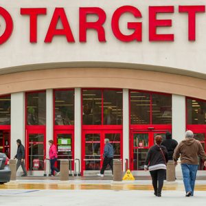 People walk toward large red doors at Target storefront, parking lot with cars and a wet floor caution sign visible.