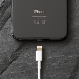 iPhone rests on dark slate surface with a white lightning cable positioned below, poised for connection.