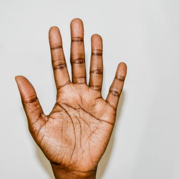 A hand is raised, open with fingers spread, against a plain, light-colored background.