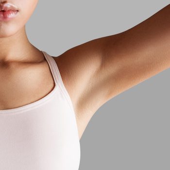 Person raises arm, wearing a sleeveless top, against a plain gray background.