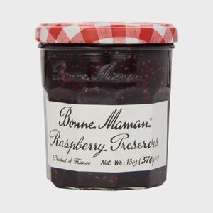 A jar stands closed, containing raspberry preserves, with a red and white checkered lid and label reading 