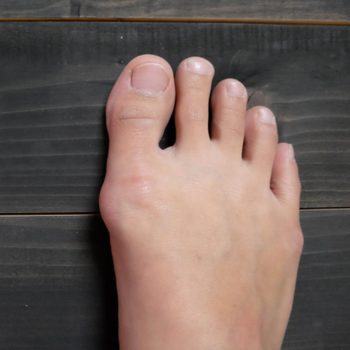 A left foot rests on a dark wooden floor, displaying natural toes and skin texture.