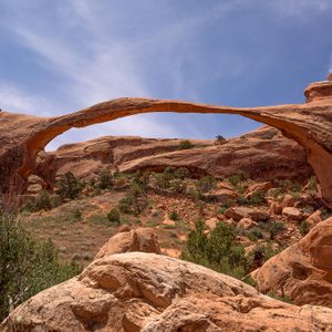 Rock arch spans between cliffs, surrounded by desert vegetation under a clear blue sky.