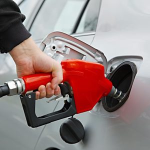 A red gas nozzle being inserted into a silver car's fuel tank at a gas station.