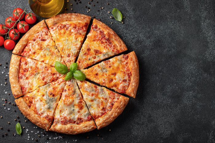 Delicious Italian pizza four cheeses with Basil, tomatoes and olive oil on a dark concrete table. Top view with copy space. Flat lay