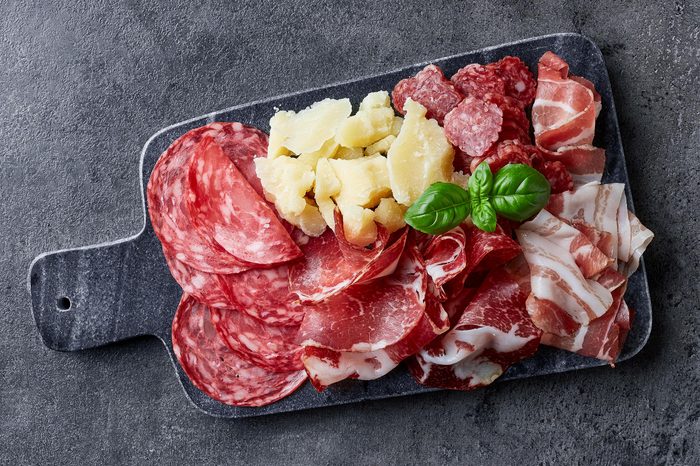 Marble cutting board with prosciutto, bacon, salami and cheese on dark stone background. From top view