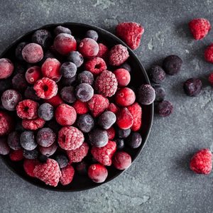 Frozen mixed berries sit in a black bowl, scattered over a dark stone surface.