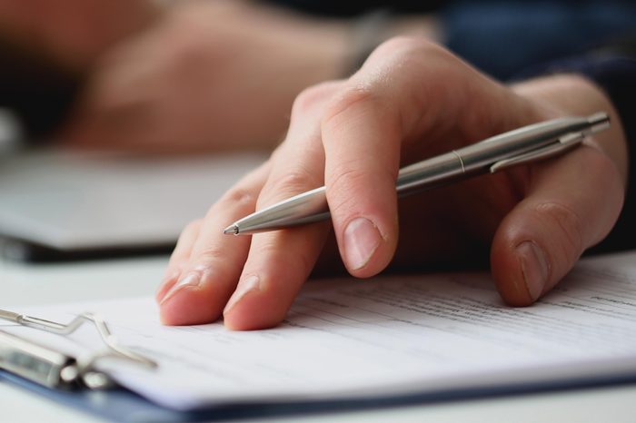 Hand of businessman in suit filling and signing with silver pen partnership agreement form clipped to pad closeup. Management training course, some important document, team leader ambition concept