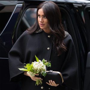 A person holds a small bouquet and a clutch, exiting a vehicle. The person is wearing a black coat with decorative buttons.