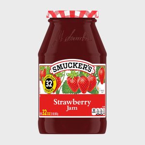 Jar holds strawberry jam, featuring bright strawberries on label against red background, with checkered lid, stating 