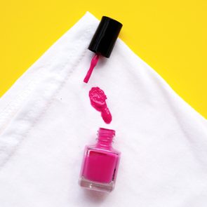 Pink nail polish spills onto a white cloth, with context set against a bright yellow background.