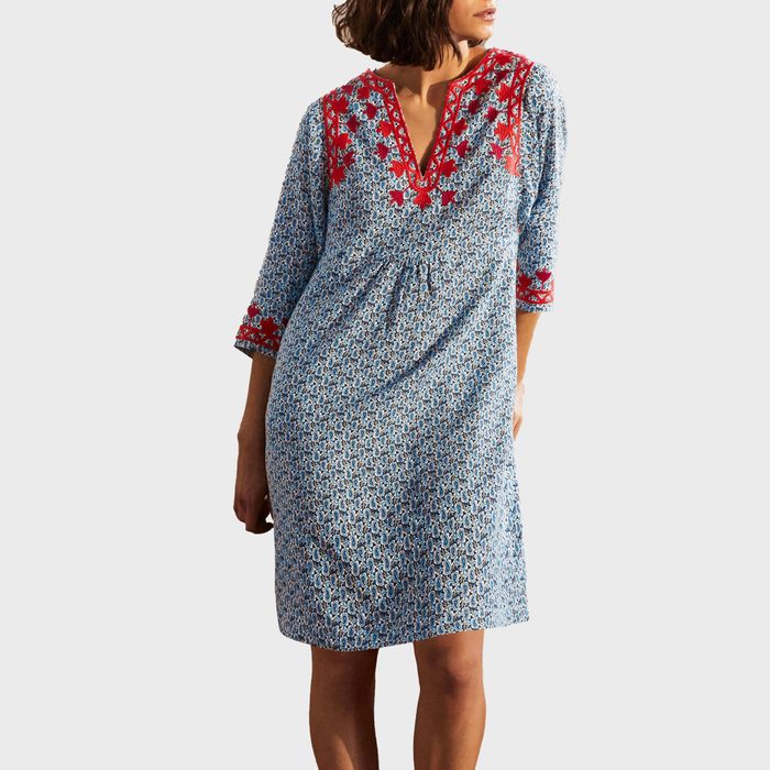 A woman models a blue-patterned dress with red embroidery, posing against a plain white background.