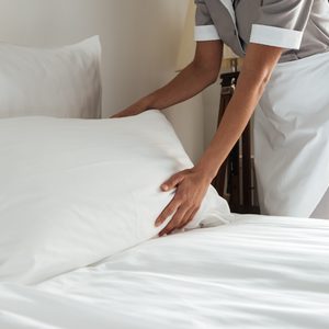 Hands arrange a pillow on a neatly made bed in a hotel room.
