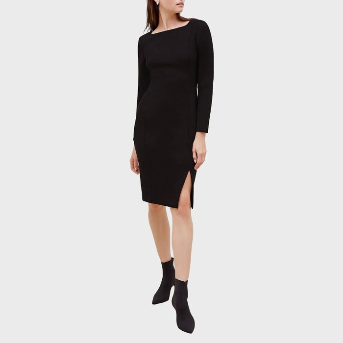 A woman models a black, long-sleeved dress with a side slit and heeled ankle boots, against a plain light background.