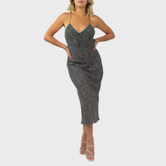 A person poses confidently, wearing a fitted, patterned dress and strappy heels, standing against a plain, light gray background.
