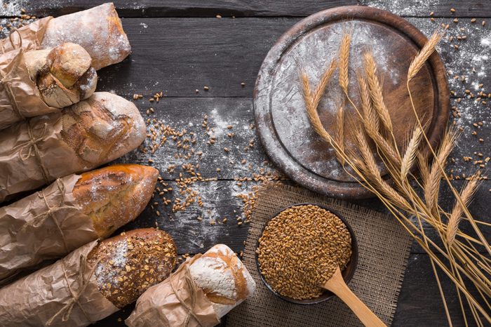 Bread background. Brown and white whole grain loaves wrapped in kraft paper composition on rustic dark wood with empty desk copy space. Baking and home bread making concept. Soft toning