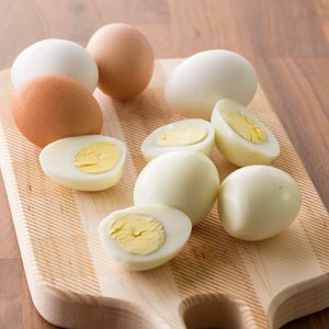 Eggs rest and are sliced on a wooden cutting board, with shells and insides visible in a kitchen setting.
