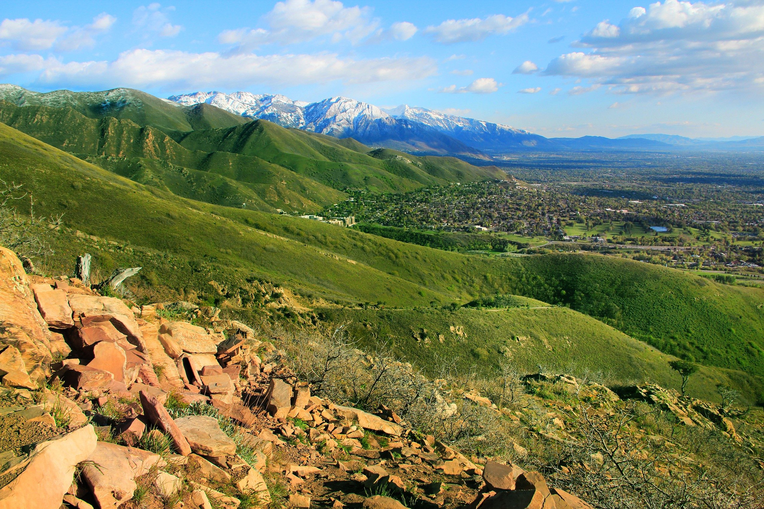 Nature: Landscape of Green Mountain and Orange Rocks with Cityscape and Snow Mountain in Background. Cloudy Blue Sky Daytime.