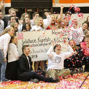 Group celebrates, holding large check, surrounded by confetti in a gymnasium. Check text: 