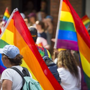 Rainbow flags wave amidst a crowd of people participating in a colorful outdoor gathering or parade.
