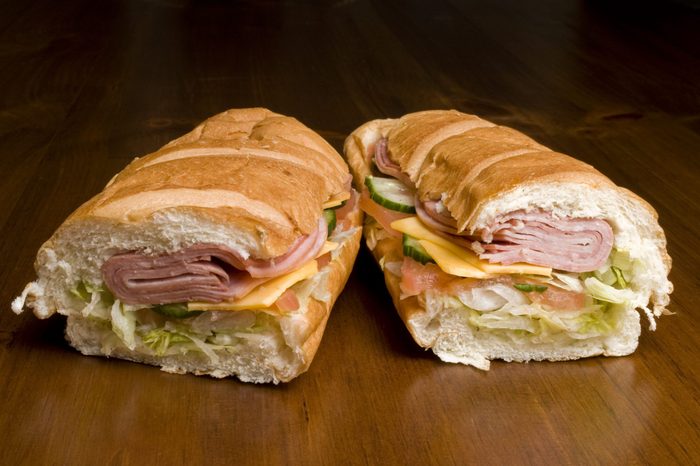 Two halves of a submarine sandwich filled with meat, cheese, cucumber, and lettuce.