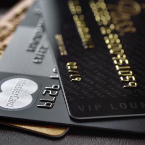 Stacked credit cards, featuring embossed details, sit on a dark surface. Prominent logos include Mastercard, and numbers are visible on black and gold cards.