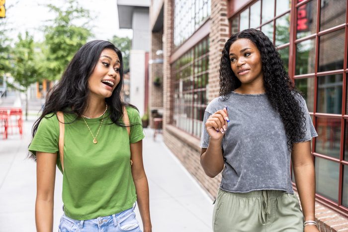 Two young women walking down urban street and laughing