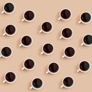 White coffee cups filled with dark liquid are arranged in a diagonal grid pattern on a beige background.