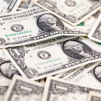 US one-dollar bills scattered, featuring George Washington's portrait, amidst overlapping currency.