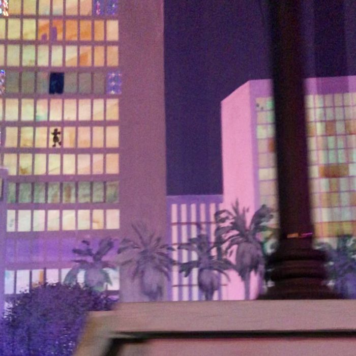 Building lights flicker at night, palm trees silhouetted in the foreground, creating an urban, tropical atmosphere.