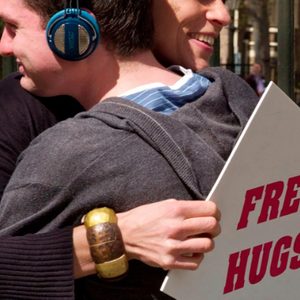 Two people hug; one wears headphones, holding a 