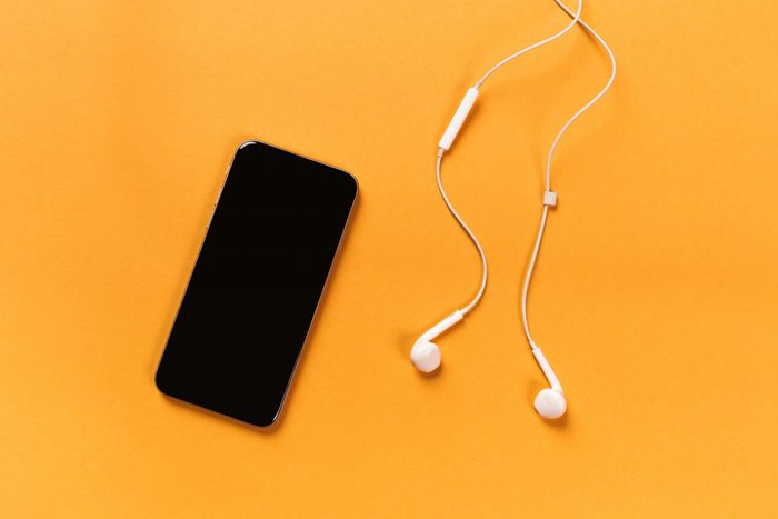 Mobile phone with white earphones on colour backgroung, top view