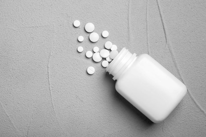 Container with pills on grey background, flat lay