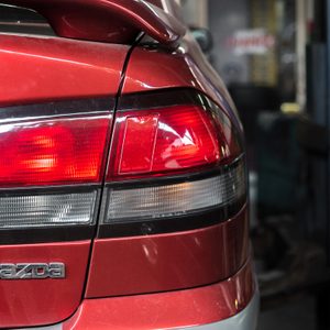 A red car's rear with tail lights on, located in a garage, showing the 