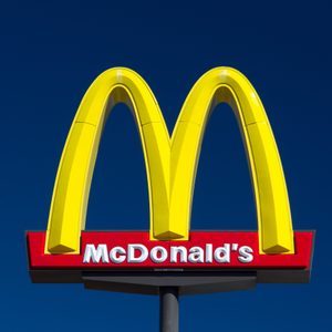 Yellow McDonald's arches stand prominently against a clear blue sky, displaying the brand name on a red background beneath the arches.