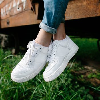 White sneakers hang as legs dangle over a rusty train in a grassy area.