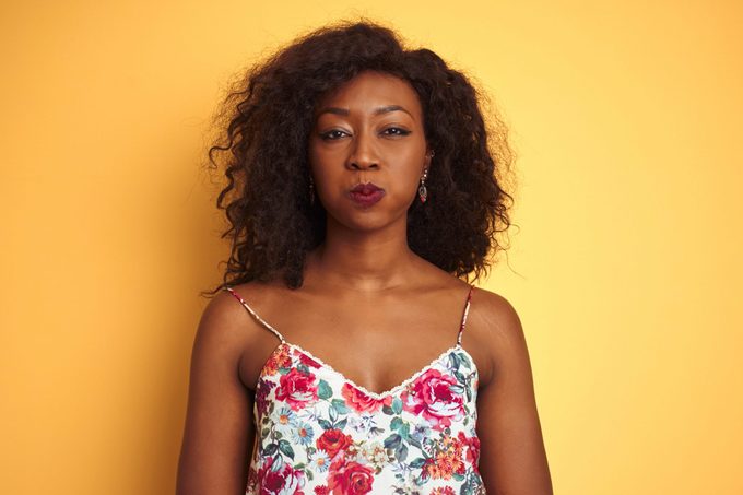 African american woman wearing floral summer t-shirt over isolated yellow background puffing cheeks with funny face. Mouth inflated with air, crazy expression.