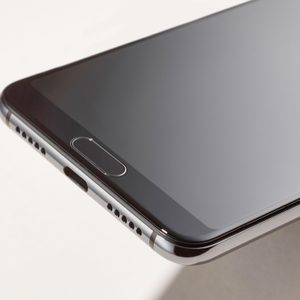 Smartphone lies on a pale surface, showcasing its sleek design, glass screen, and metal edges with speaker holes visible.