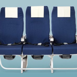 Three blue airplane seats, aligned with seatbelts fastened, on a light blue background.