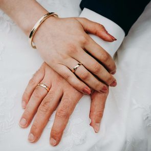 Two hands rest on each other, showing wedding rings on a lace-covered surface.