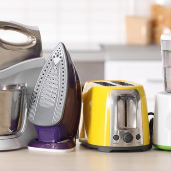 A mixer, iron, yellow toaster, and white blender sit on a kitchen countertop with a blurred background.