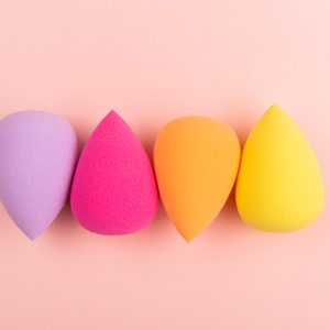 Four colorful makeup sponges arranged side by side on a soft pink background.