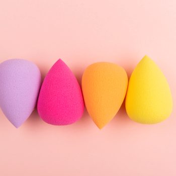Four colorful makeup sponges arranged side by side on a soft pink background.
