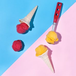 Ice cream cones rest with scoops of red and yellow ice cream on a split blue and pink background.