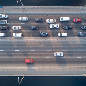 Cars are moving or stationary in traffic on a multi-lane bridge over water, with streetlights and colorful railings lining the bridge's edges.